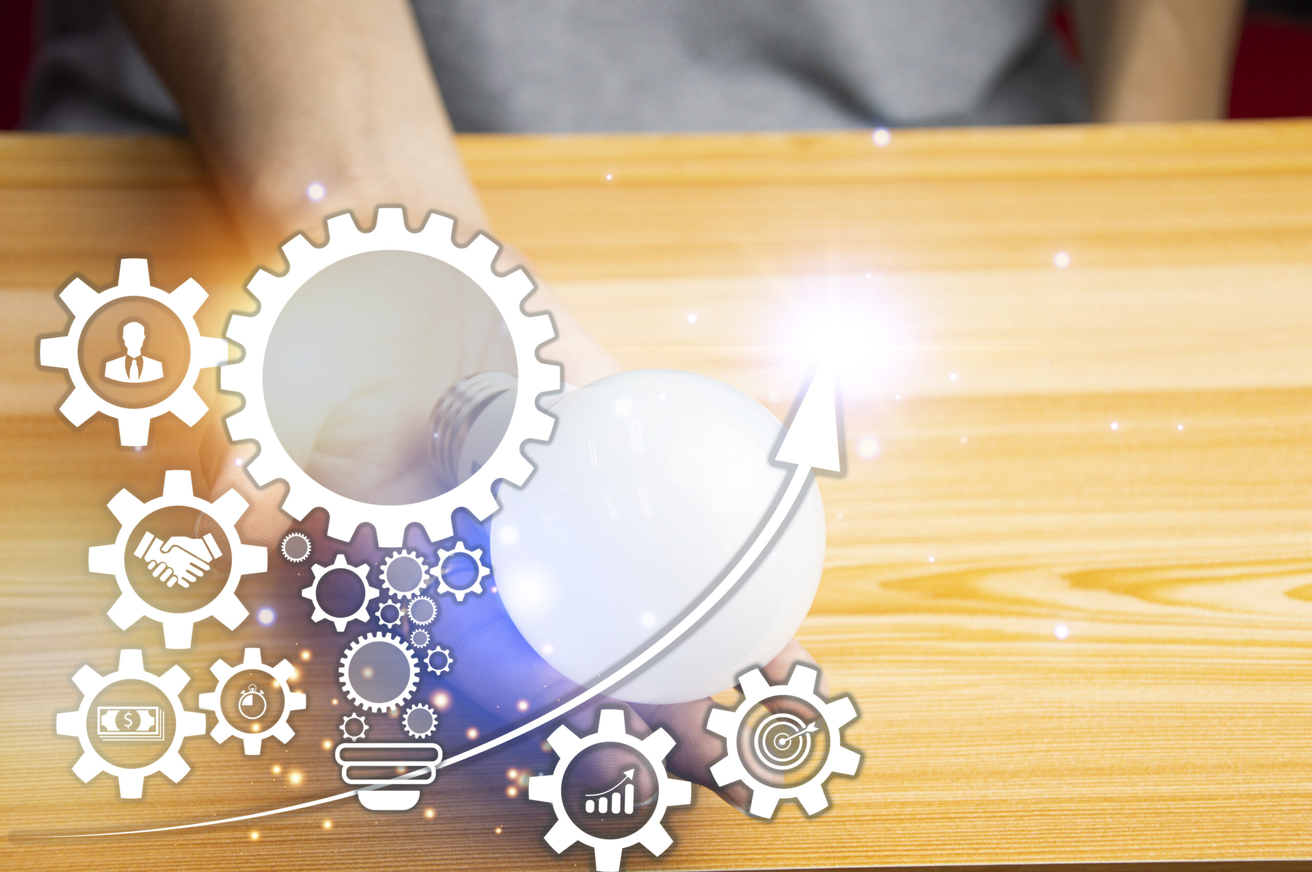 Eine Hand h&auml;lt eine leuchtende Gl&uuml;hbirne &ndash; umgeben von grafischen Symbolen wie Zahnr&auml;dern, Wachstumspfeilen und Zusammenarbeit. Das Bild visualisiert Entwicklungsfortschritt, strukturiertes Arbeiten und die kontinuierliche Qualit&auml;tsoptimierung der EXELTRA-Gr&uuml;ndungsphase.