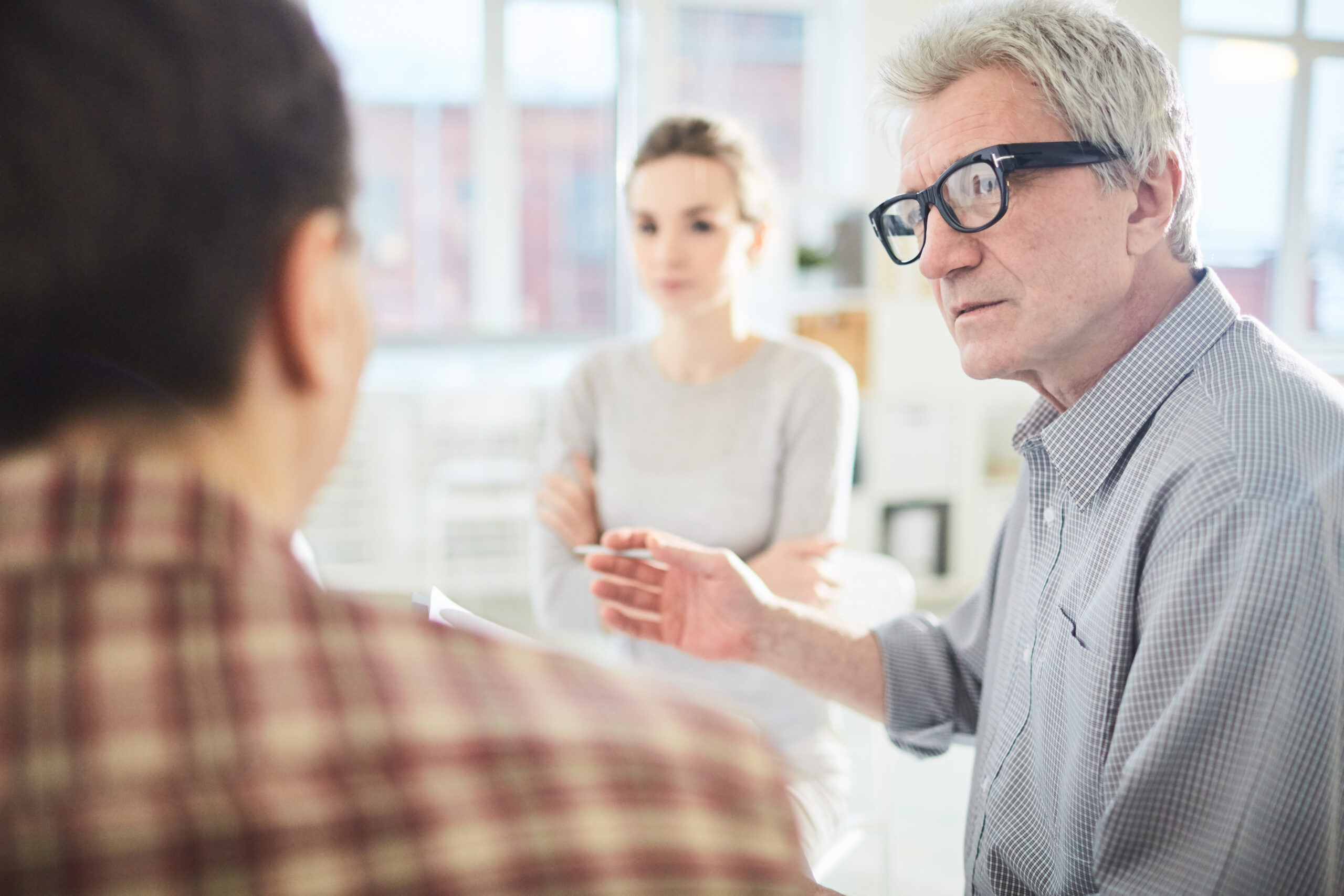 Ein erfahrener Trainer spricht konzentriert mit zwei Teilnehmenden in einem hellen, modernen Raum. Die Szene vermittelt professionelle Beratung, fachliche Expertise und pers&ouml;nliche Begleitung.
