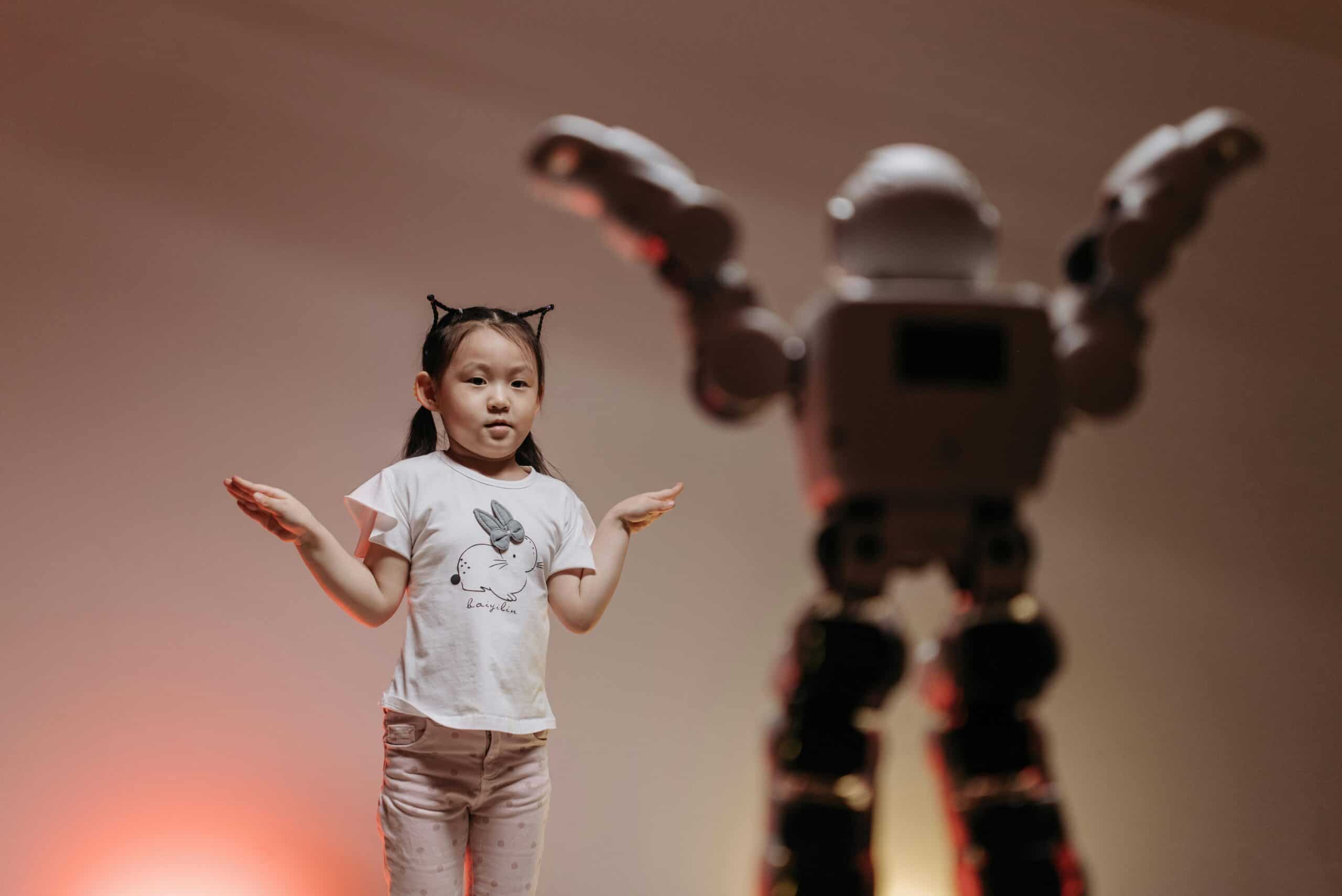 Ein Kind steht mit erhobenen Armen vor einem gro&szlig;en Spielroboter, der ebenfalls die Arme hebt.
