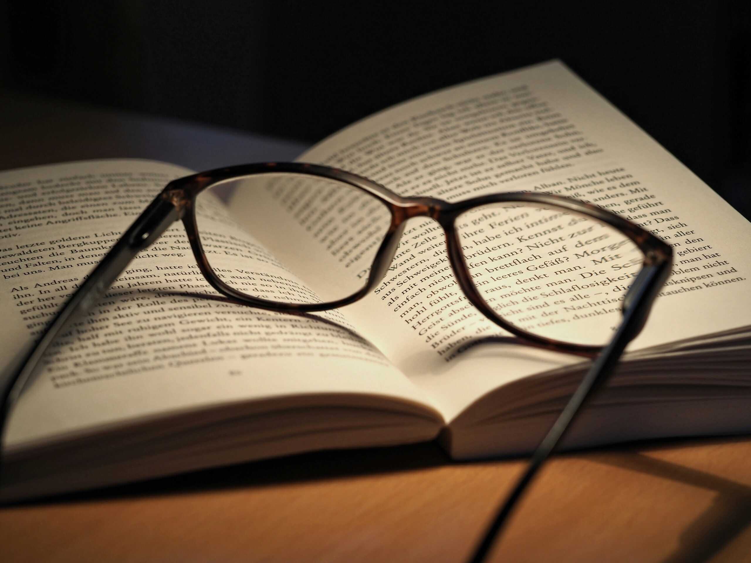 Eine Brille liegt auf einem aufgeschlagenen Buch.